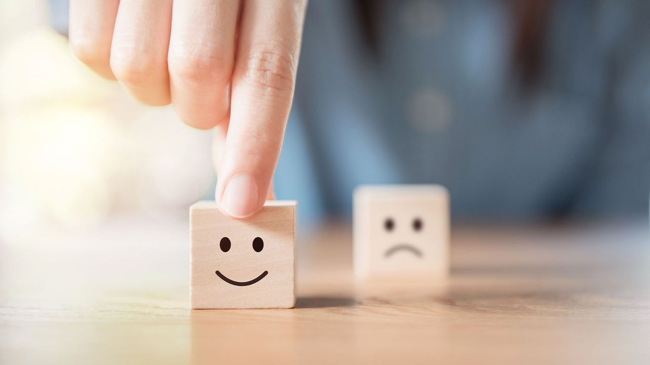 Una mano tomando cubo de madera con carita sonriente en vez del cubo de madera con cara triste que se encuentra detrás.​​ 
