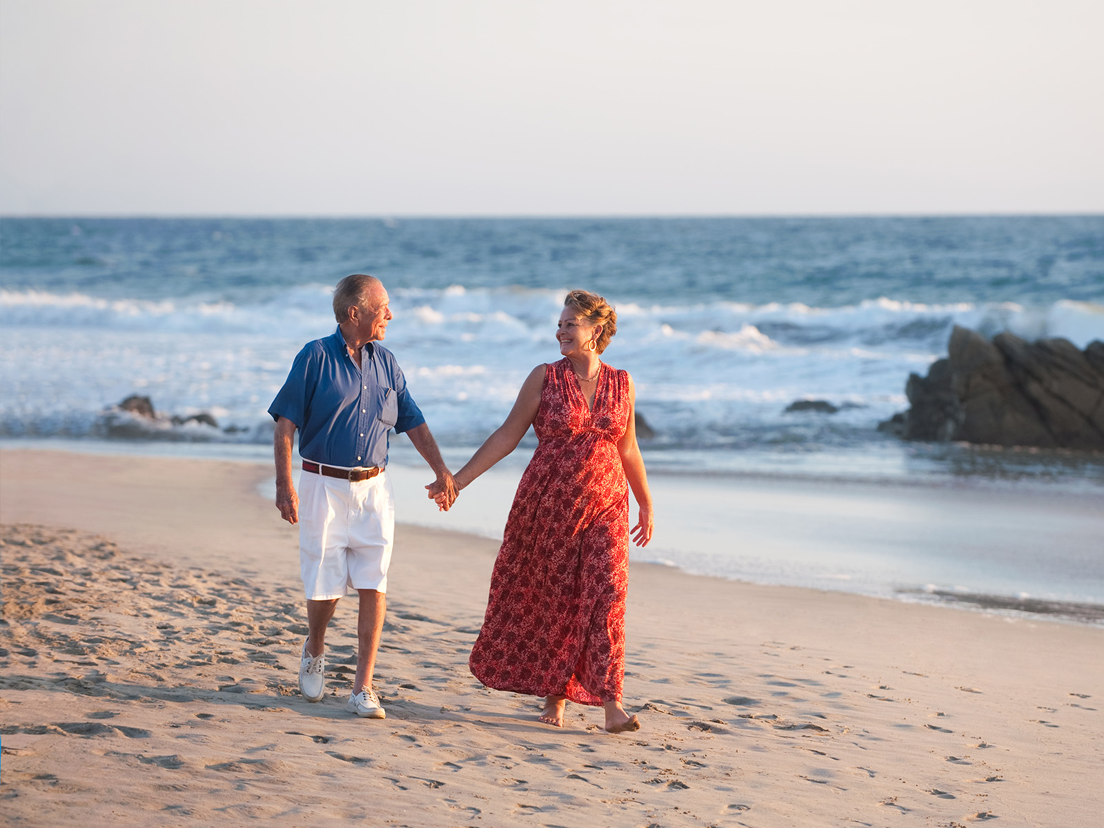 Pareja adulta caminando de la mano en la playa.​​ 