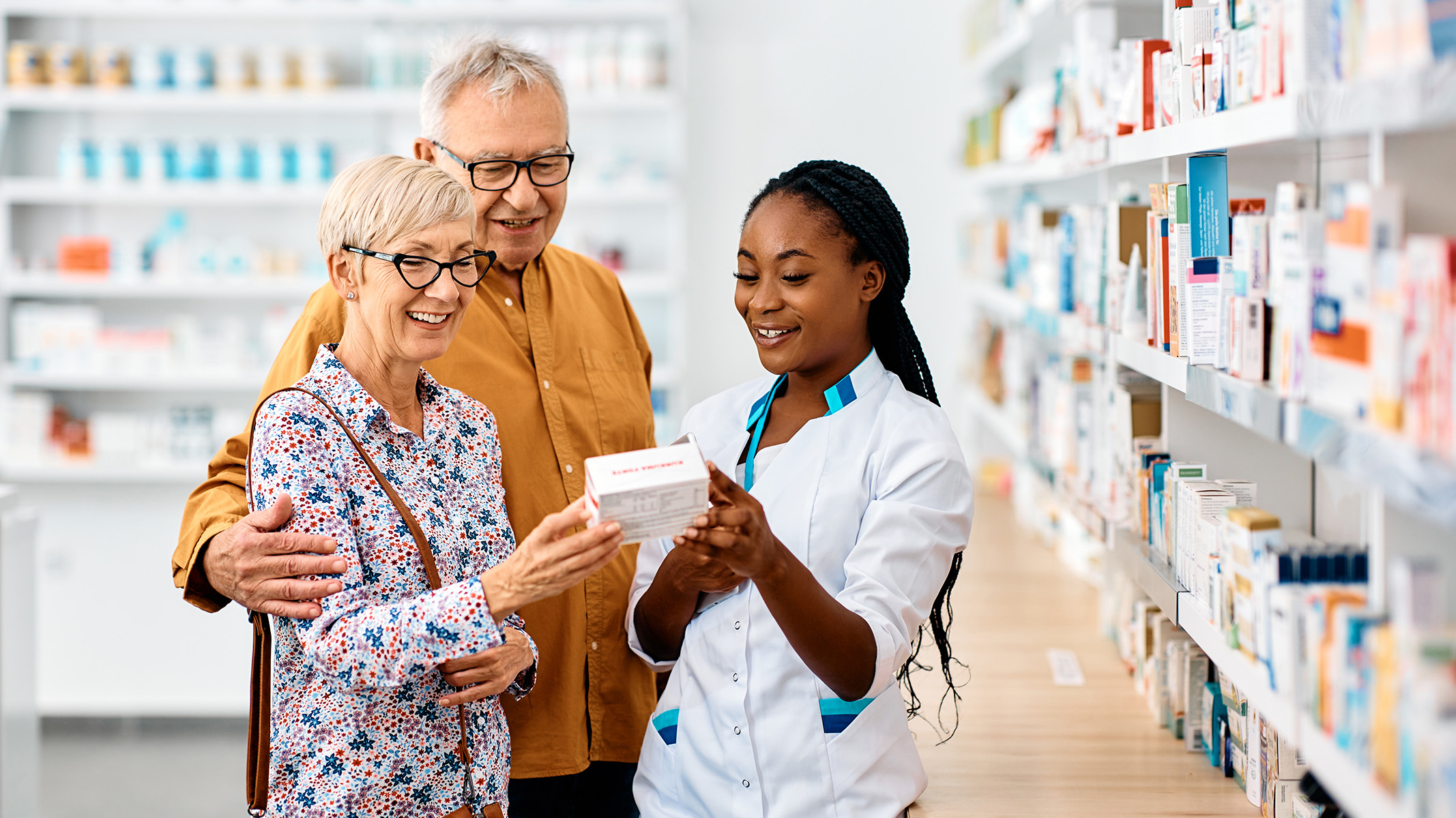 Farmacéutico muestra opciones de medicamentos a una pareja de personas de la tercera edad.​​ 
