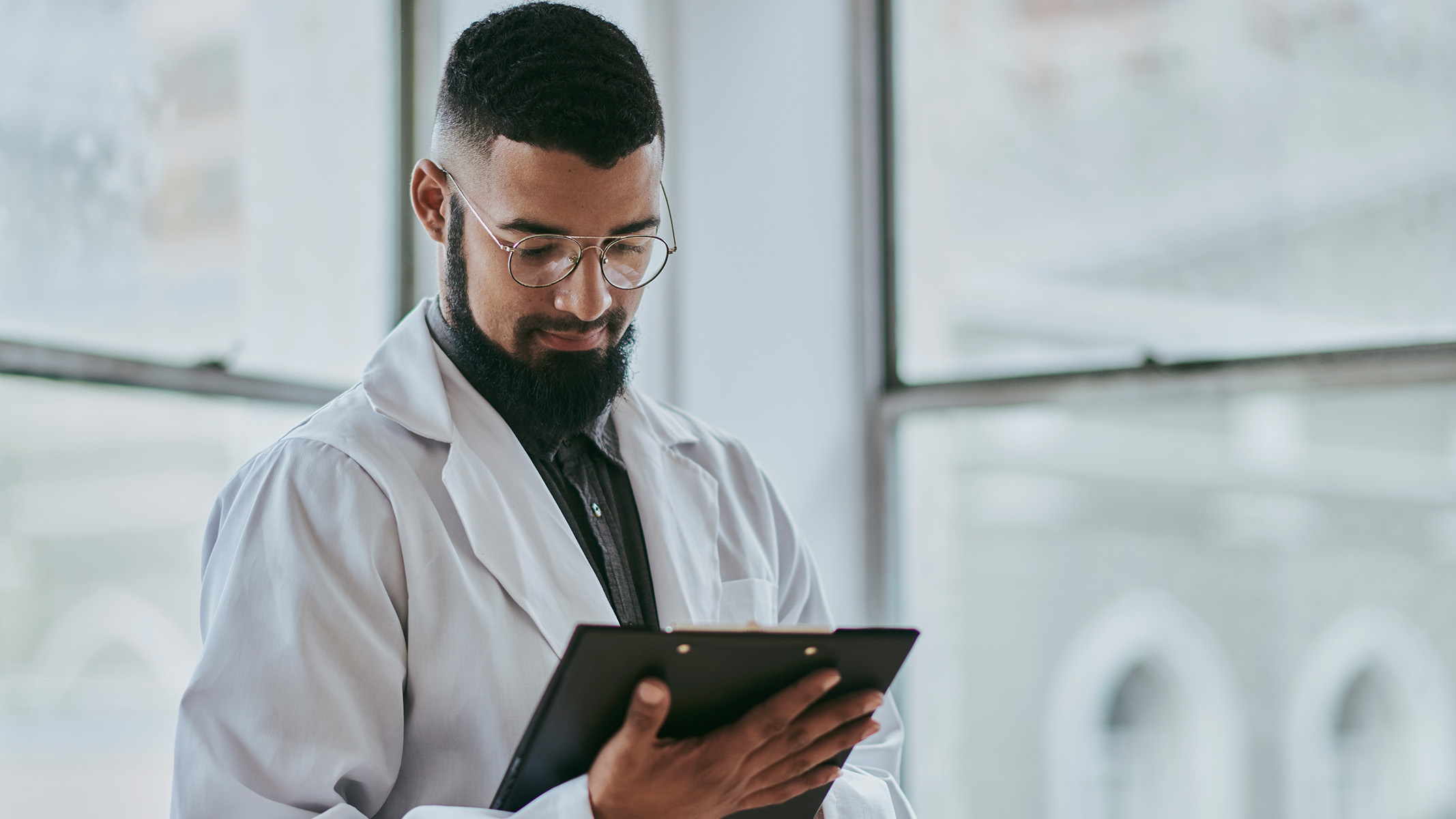Un médico joven está de pie mirando un documento médico.​​ 