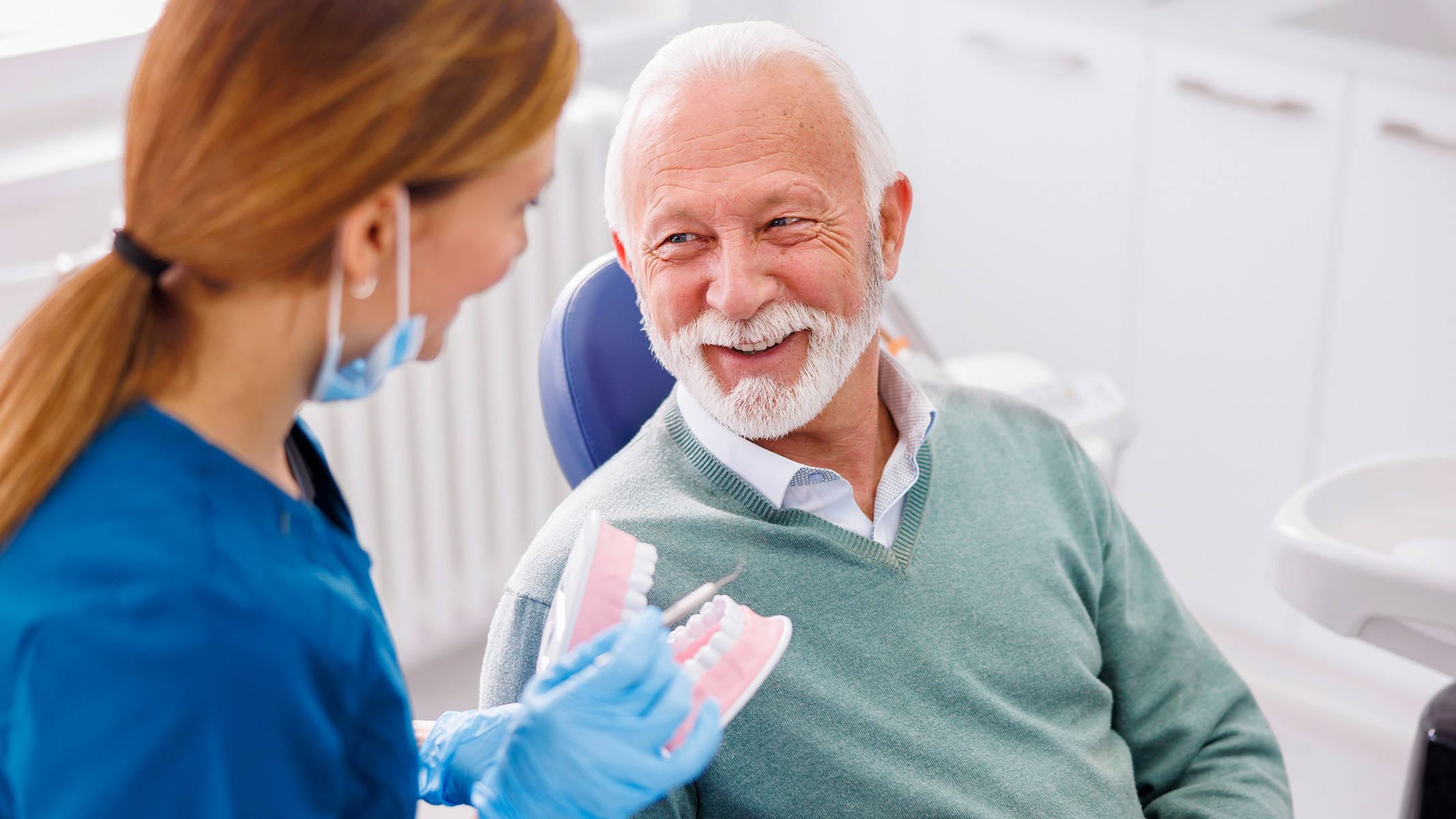 Una dentista le muestra un modelo de dentadura postiza a un paciente de la tercera edad.​​ 
