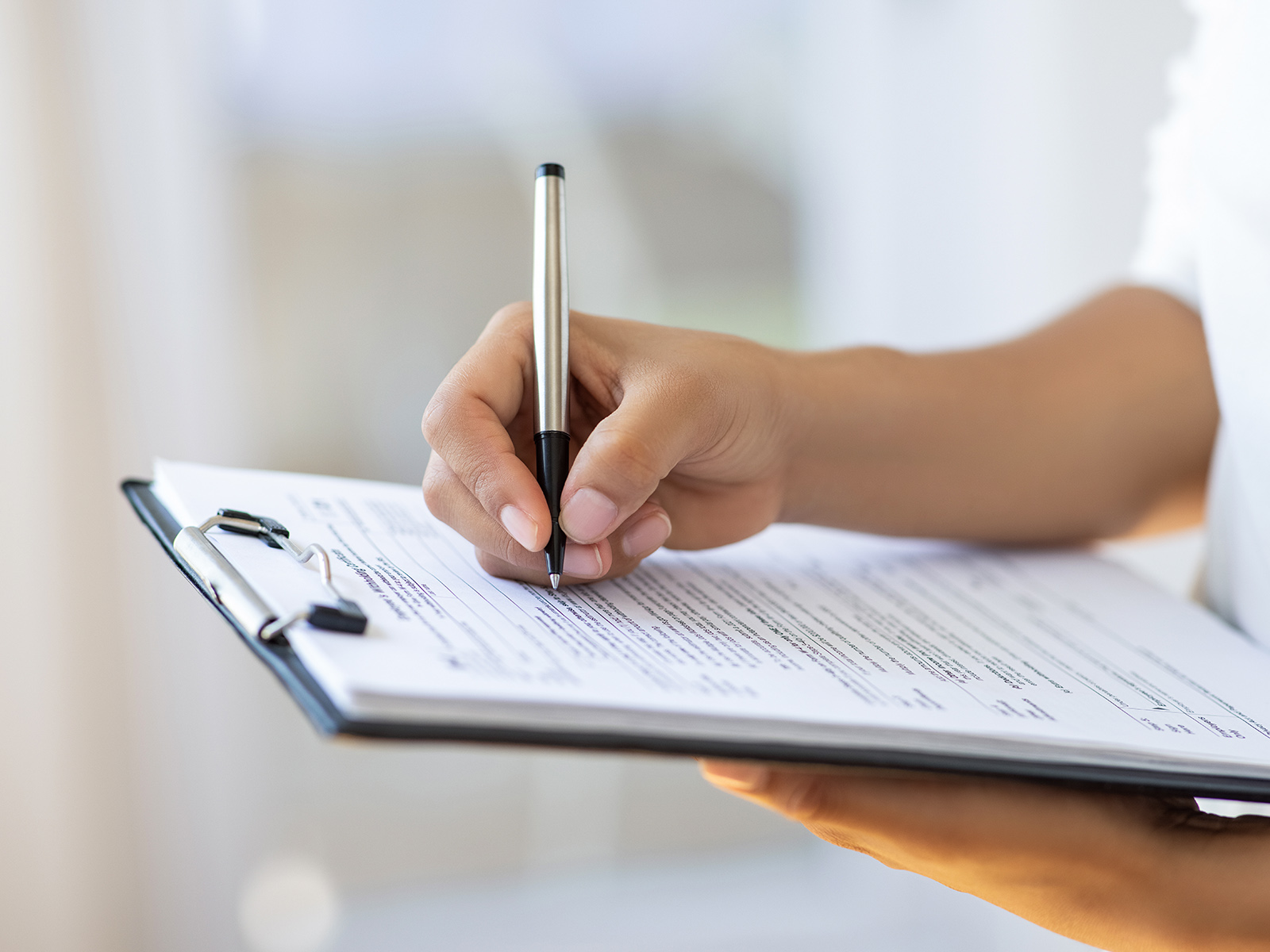 La mano de una persona que está completando un formulario sujeto a un portapapeles​​ 