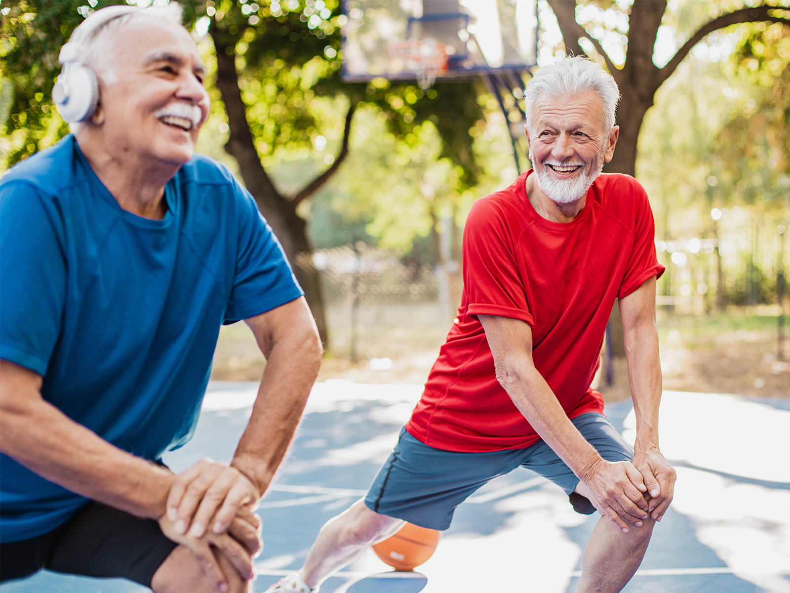 Hombres mayores haciendo ejercicios de estiramiento y sonriendo en el exterior.​​ 