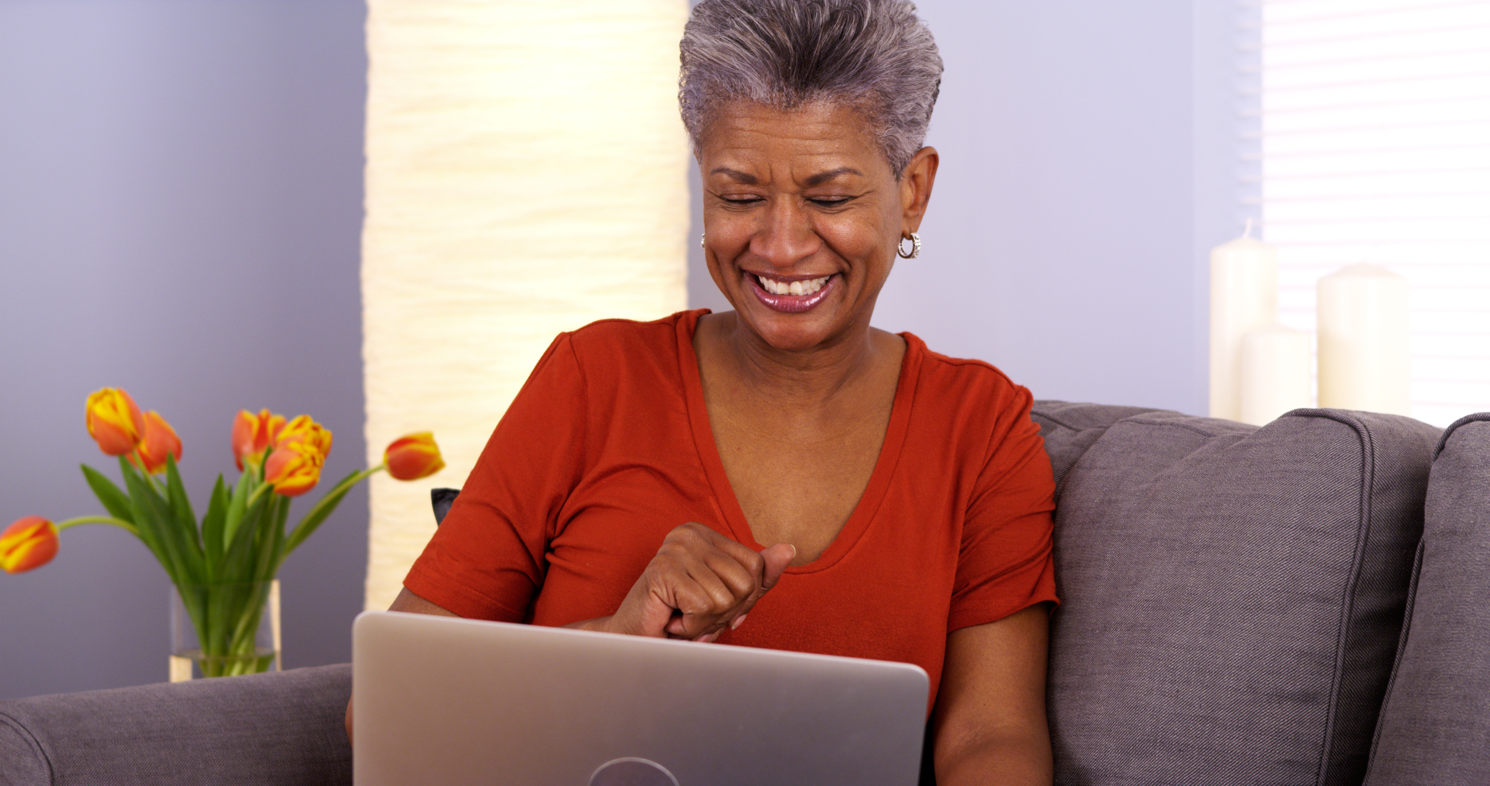 Mujer mayor sonriendo al computador portátil​​ 