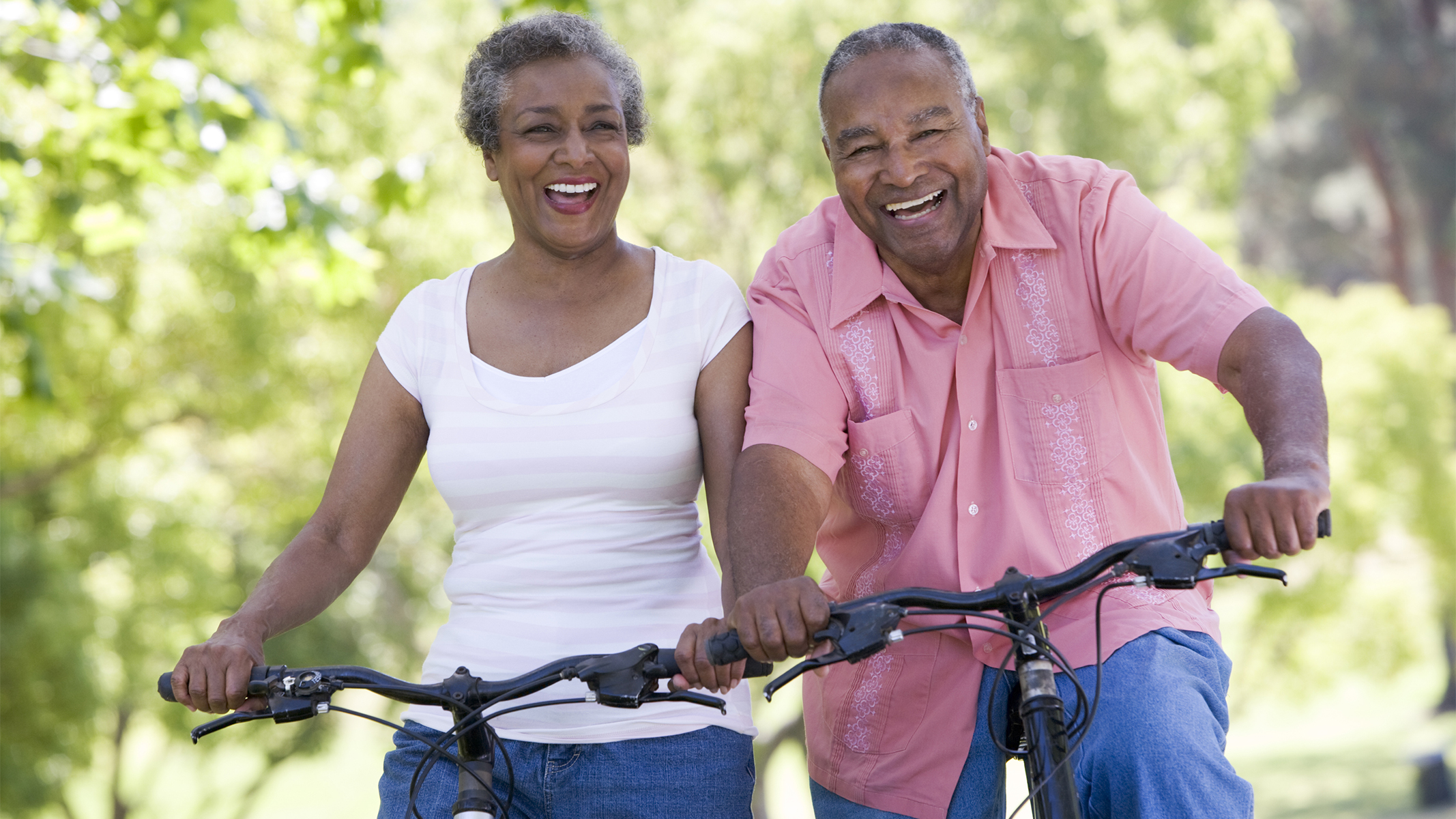 Pareja mayor sonriendo mientras andan en bicicleta.​​ 