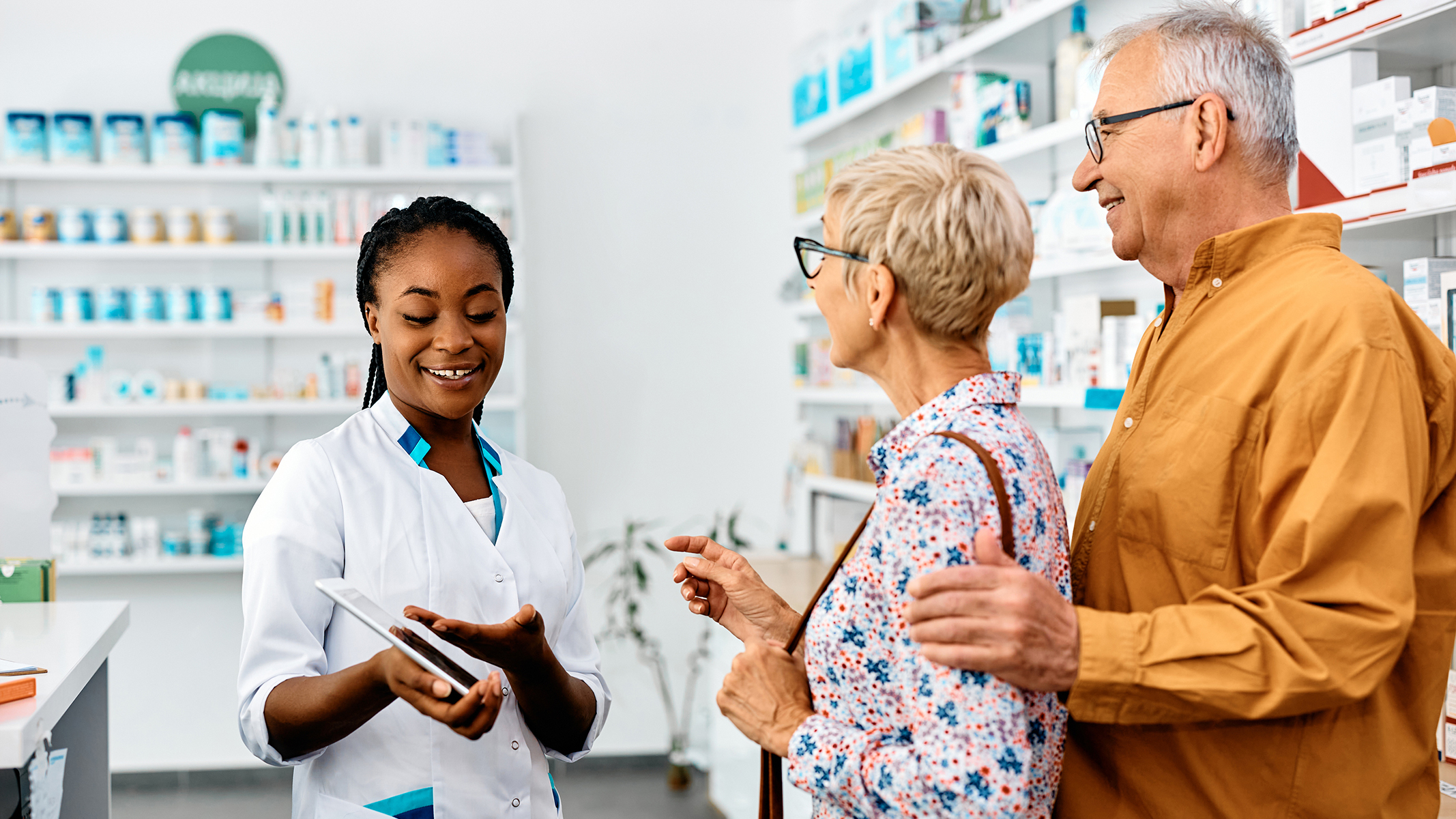 Pareja de personas mayores hablando con una farmacéutica en una farmacia.​​ 