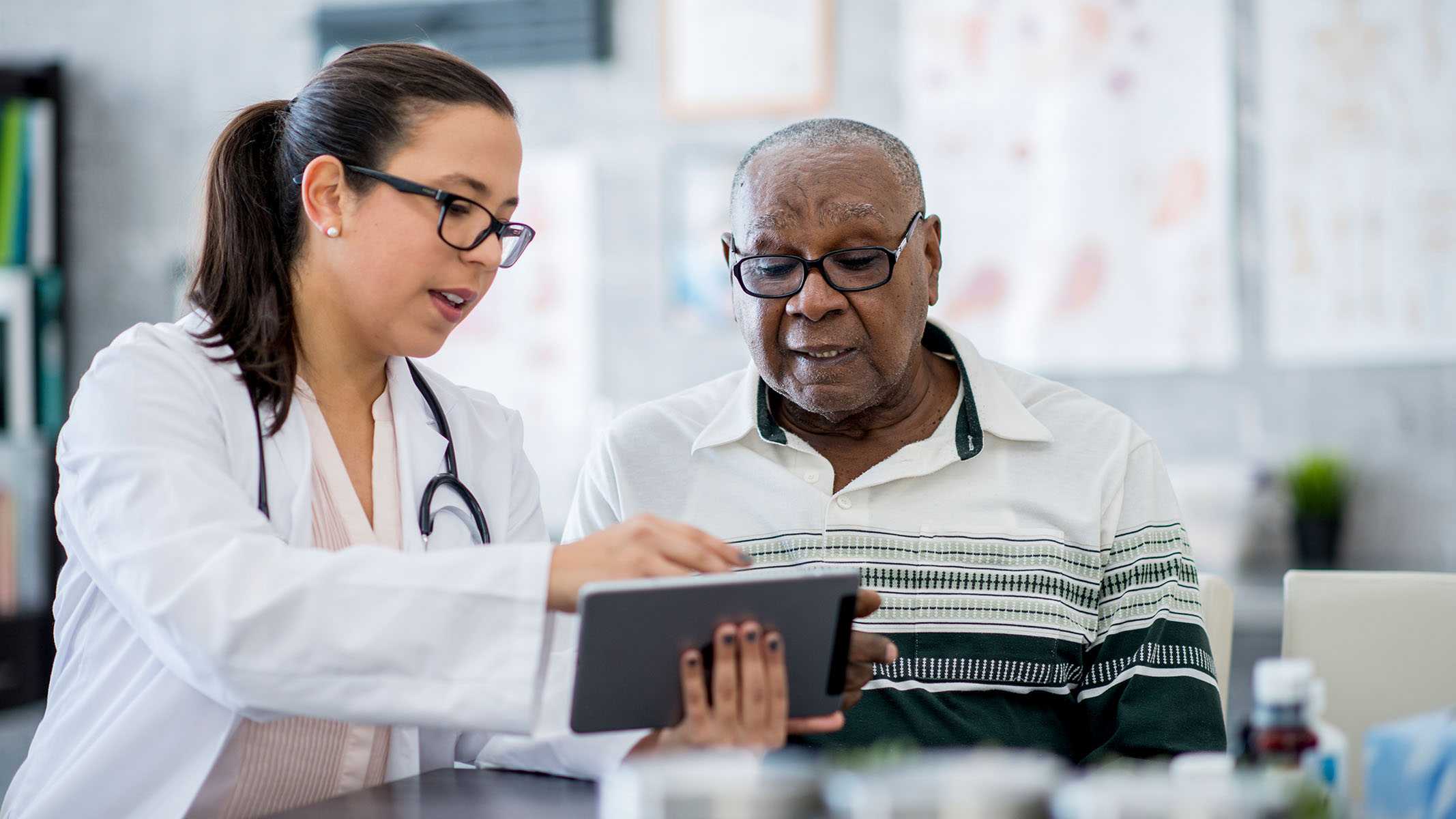Médico señalando una tablet y hablando con un paciente mayor​​ 