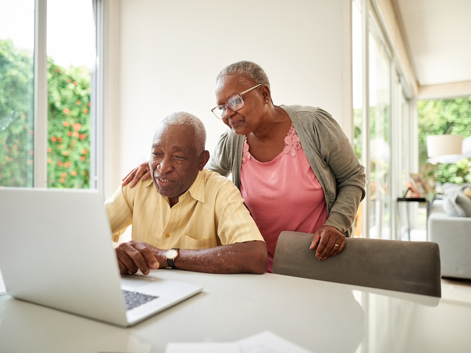 Pareja de personas mayores en casa mirando un computador portátil.​​ 