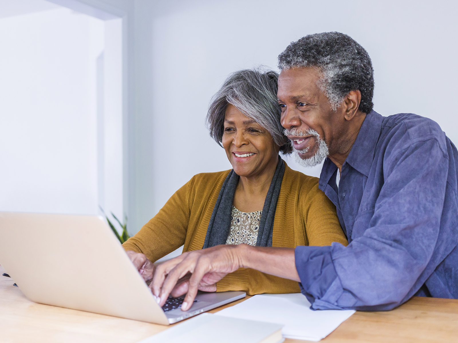 Pareja mayor sonriendo mientras usan un computador portátil.​​ 