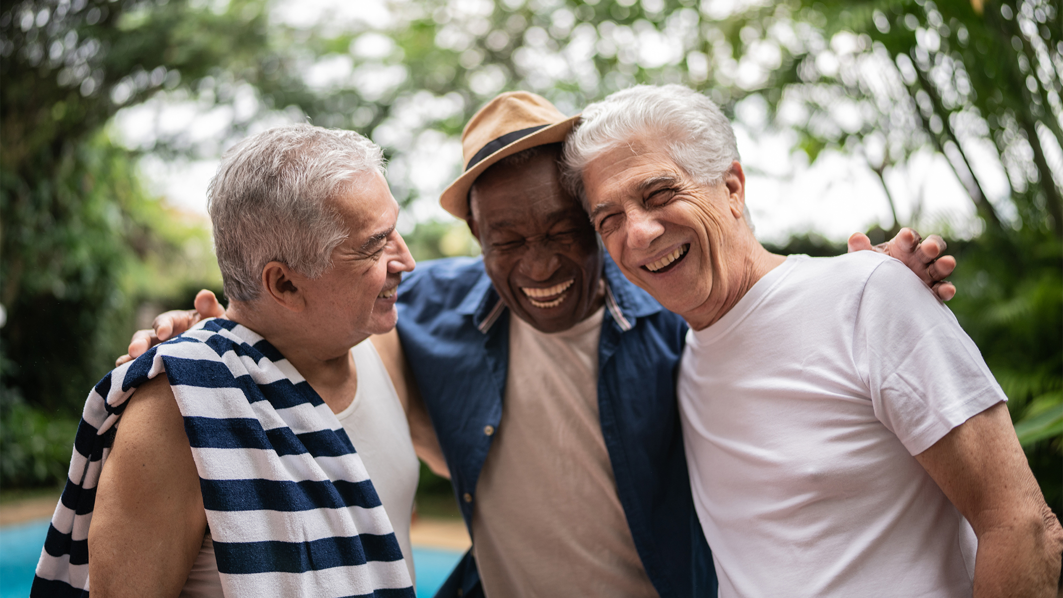  Tres hombres mayores sonriendo junto a la piscina.​​ 