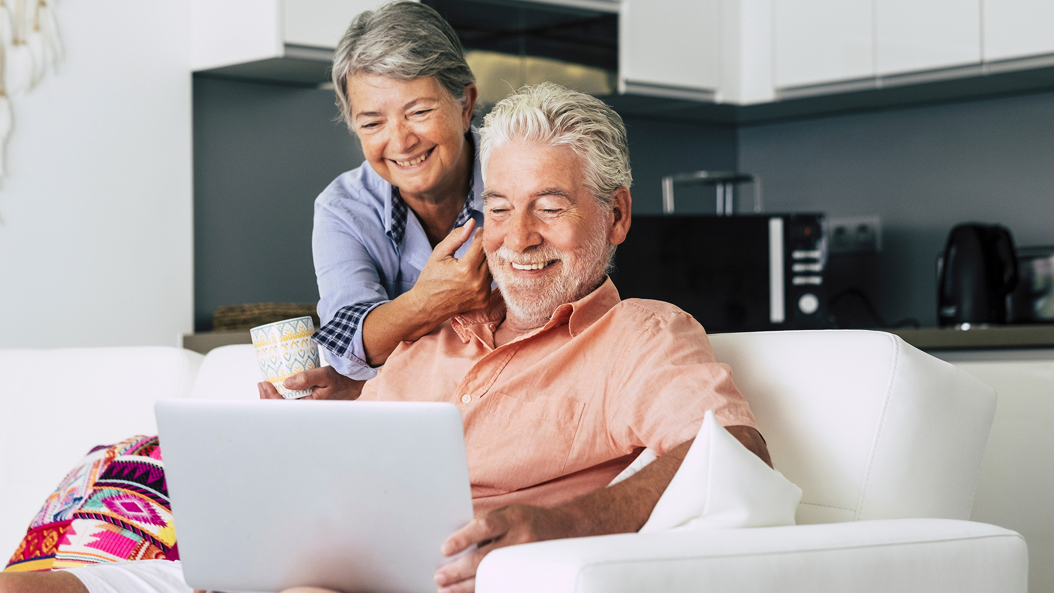 Pareja de personas mayores sonriendo y mirando un computador portátil​​ 