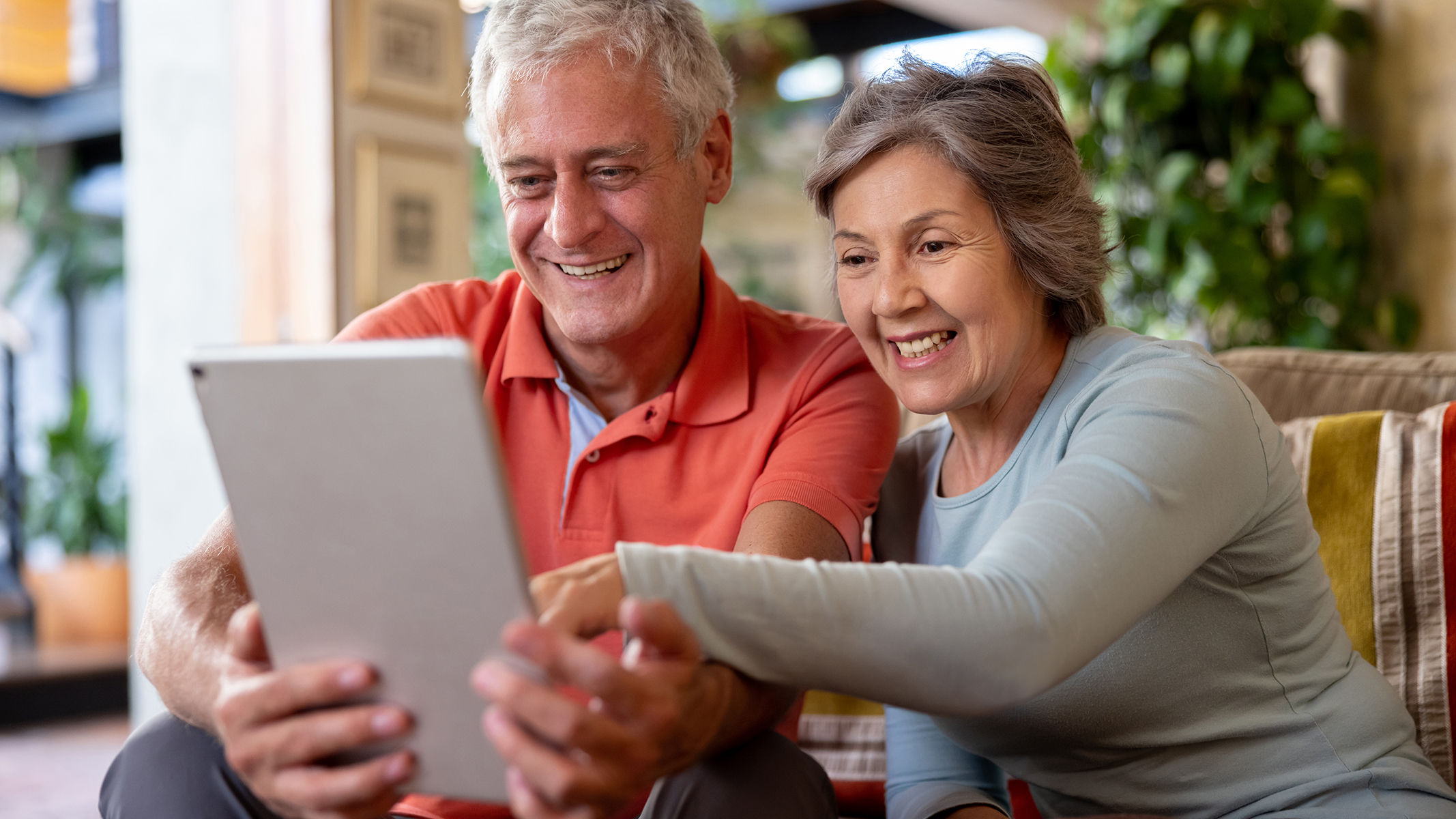 Pareja mayor sonriendo sentada mirando y señalando una tablet.​​ 