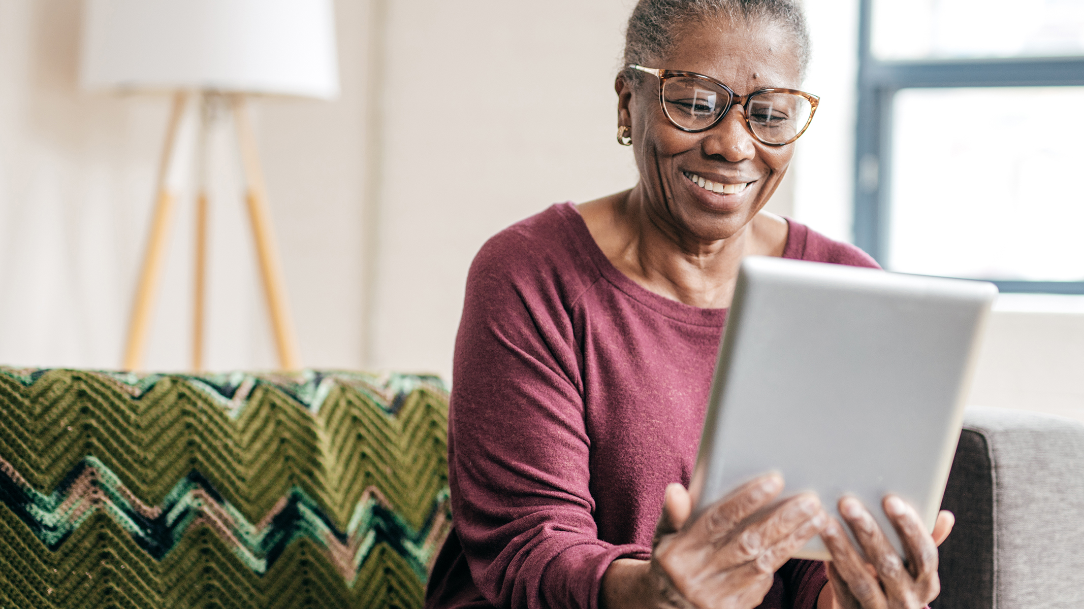 Mujer mayor sonriendo sentada y sosteniendo una tablet.​​ 