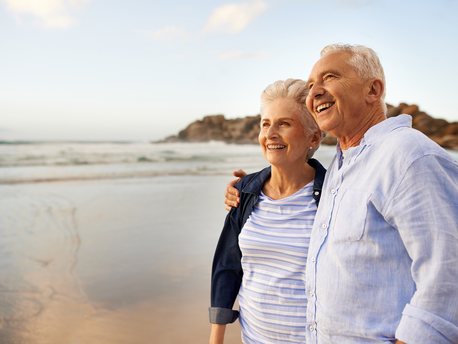 Pareja de personas mayores sonriendo en la orilla de la playa.​​ 