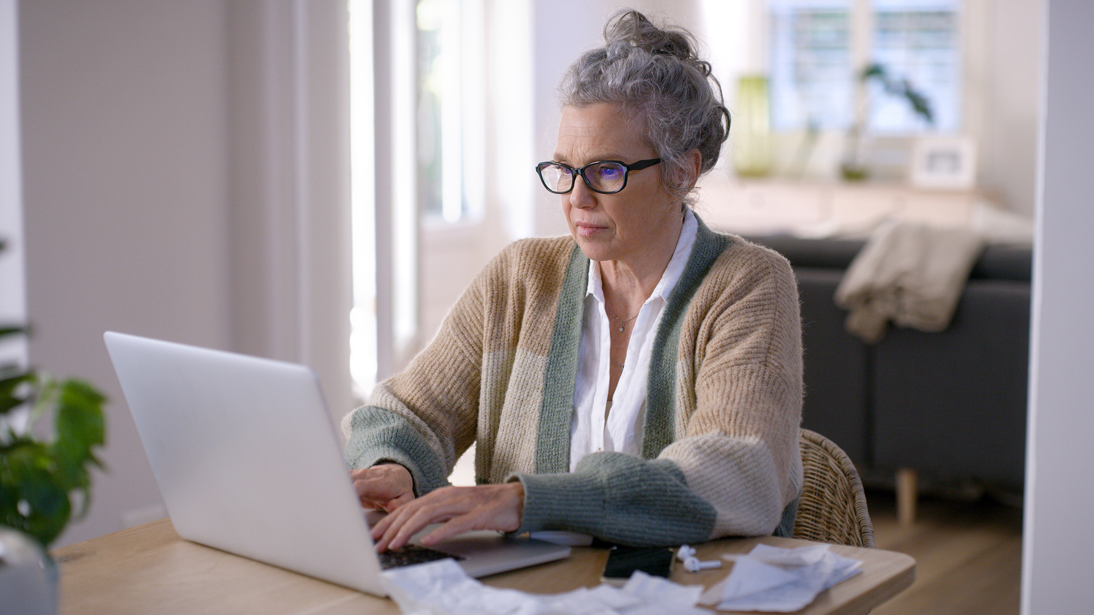 Mujer mayor trabajando en un computador portátil sentada a la mesa​​ 