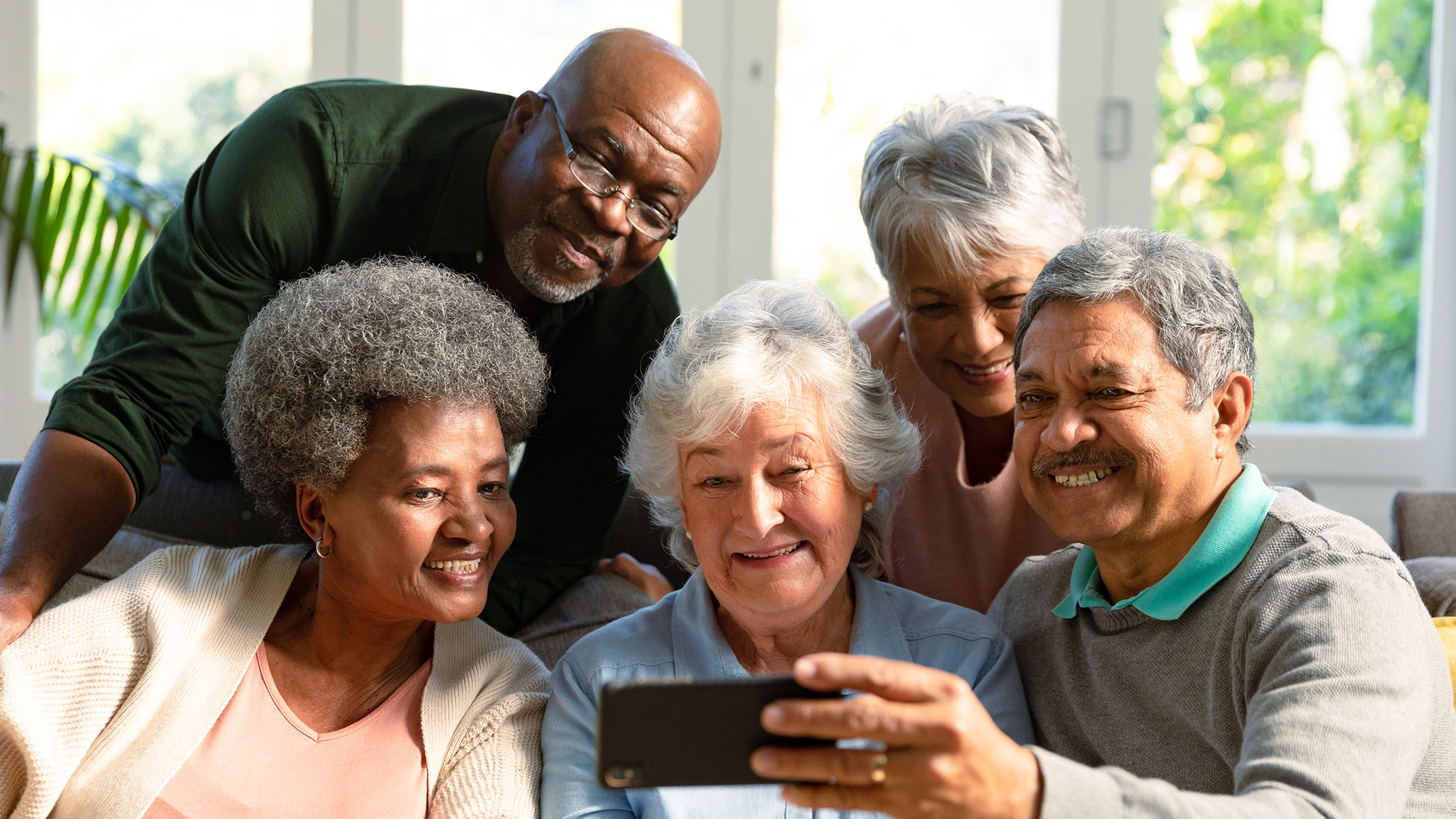 Un grupo de personas de la tercera edad sentado en un sofá mientras miran un smartphone.​​ 