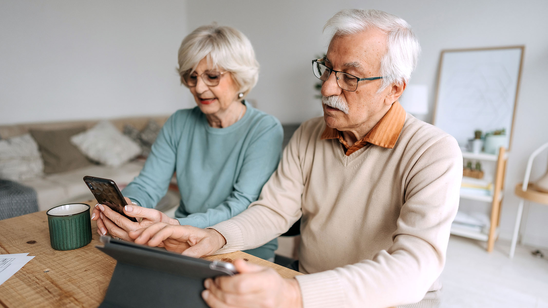 Una pareja de personas mayores usando un teléfono móvil y una tablet.​​ 